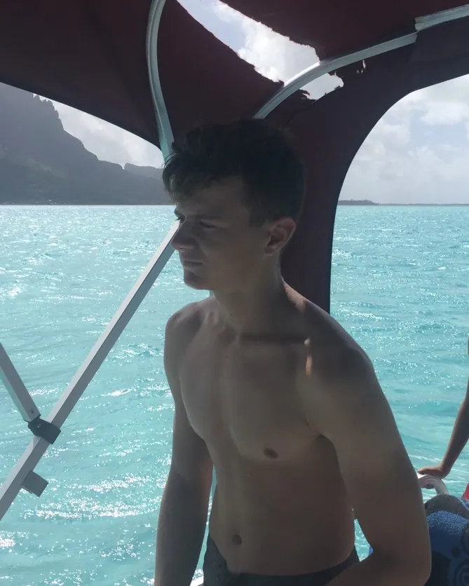 Paul adolescent, mince et torse nu, sous l'auvent d'un bateau, devant une eau turquoise.